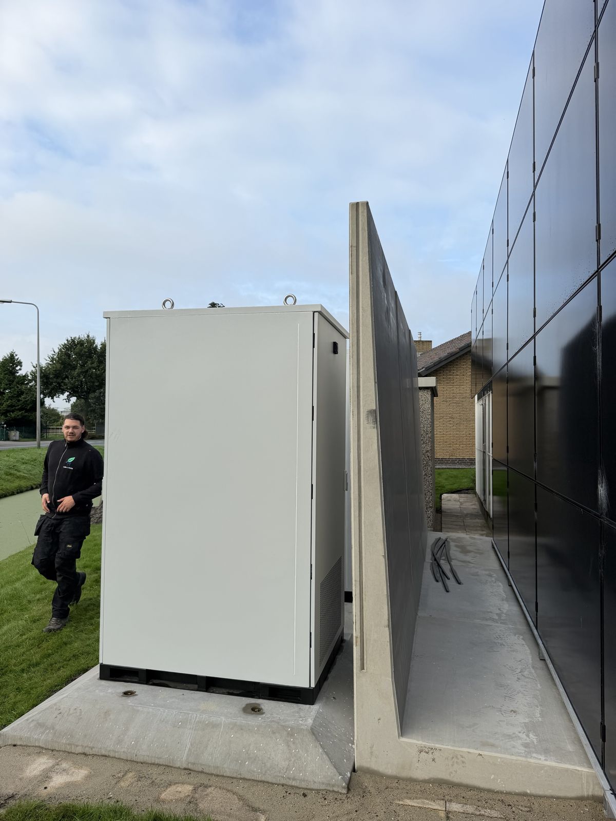 Batterijkast op de betonplaat naast de keerwand en de gevel met zonnepanelen